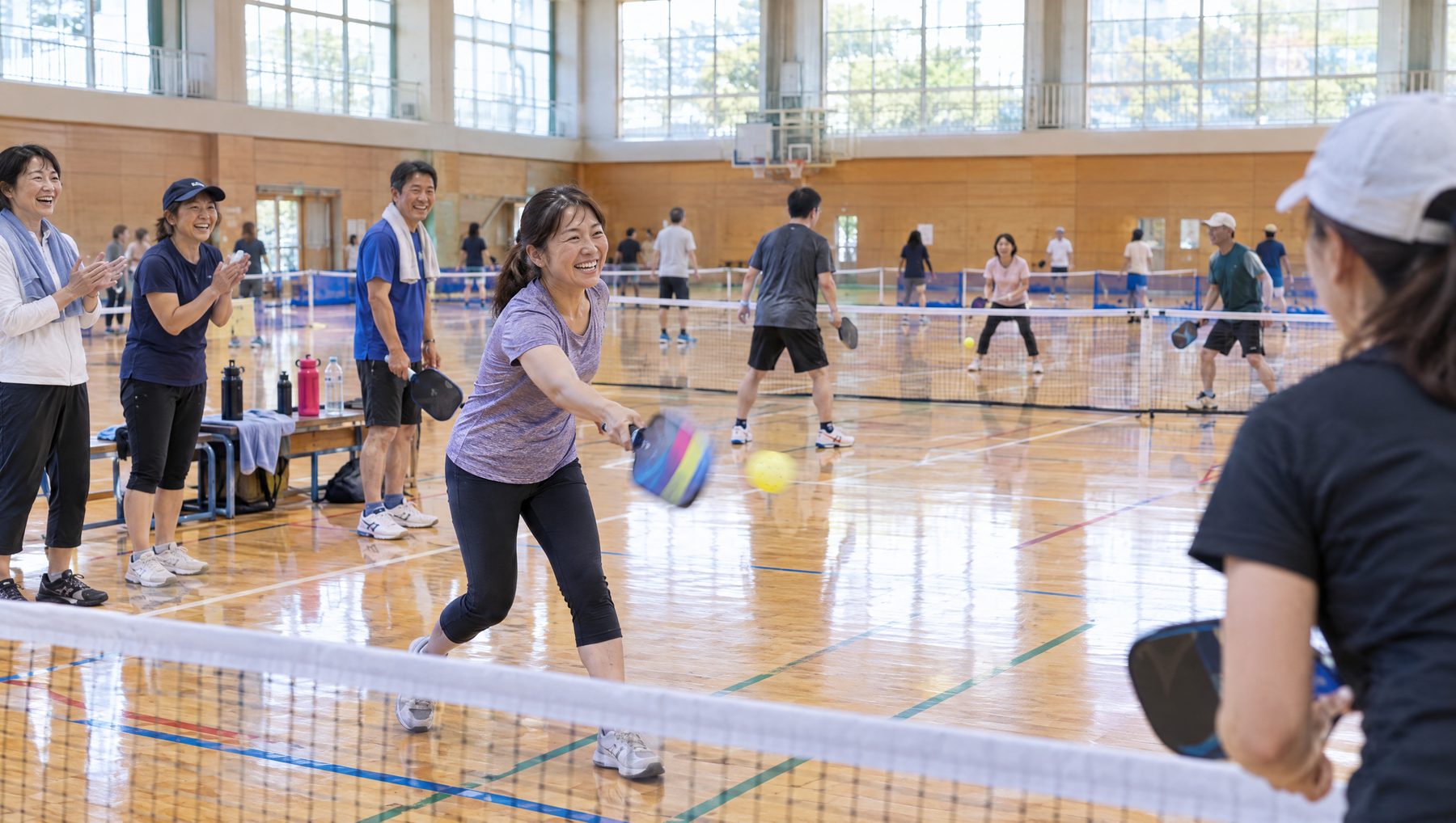 体育館で、笑いながらピックルボールのラリーをする参加者たち
